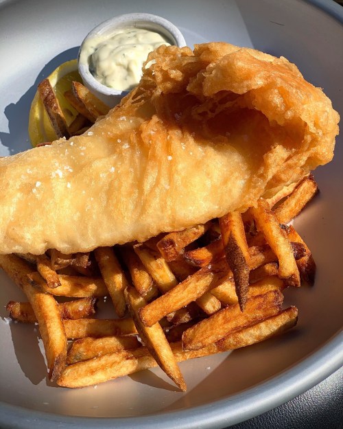 A plate of golden fried fish with crispy fries and a side of tartar sauce and lemon wedges.