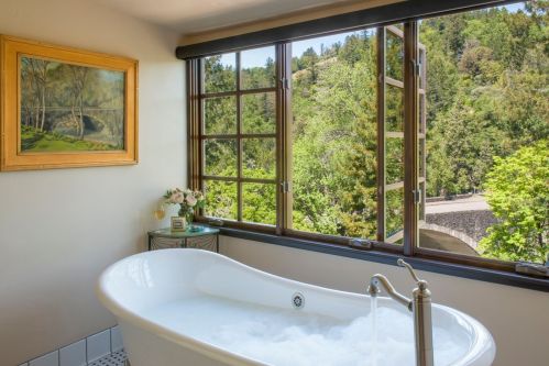 A bright bathroom with a freestanding tub and large windows overlooking a lush green landscape.