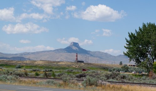 A distant mountain peak rises against a blue sky with clouds, surrounded by grassy plains and sparse trees.