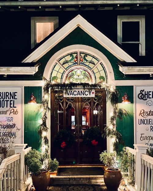 A charming hotel entrance with a stained glass window, greenery, and a "VACANCY" sign, warmly lit at night.