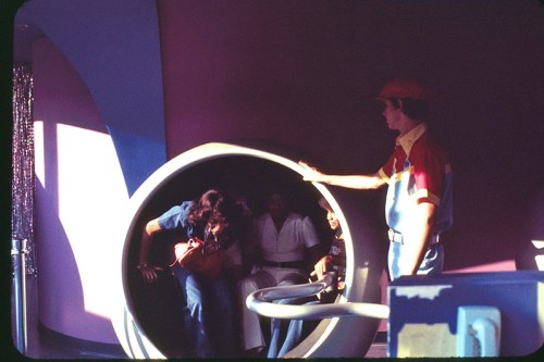 A group of people entering a circular ride while an attendant in a colorful uniform assists them.