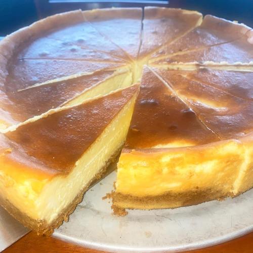 A round cheesecake with a golden-brown top, sliced into pieces, resting on a silver platter.