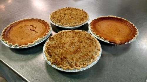 Four freshly baked pies on a metal surface: two pumpkin pies and two with crumb topping.