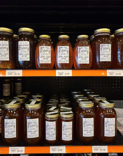 A display of various jars of honey on shelves, featuring different sizes and prices.