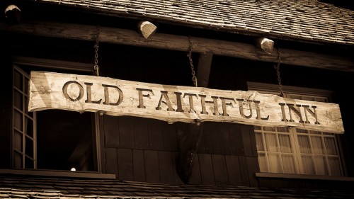 Sign for Old Faithful Inn hanging from a wooden structure, with a rustic, vintage appearance.