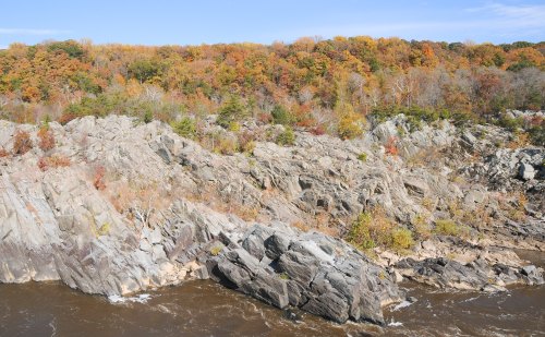 Rocky riverbank with autumn foliage in vibrant colors, under a clear blue sky.