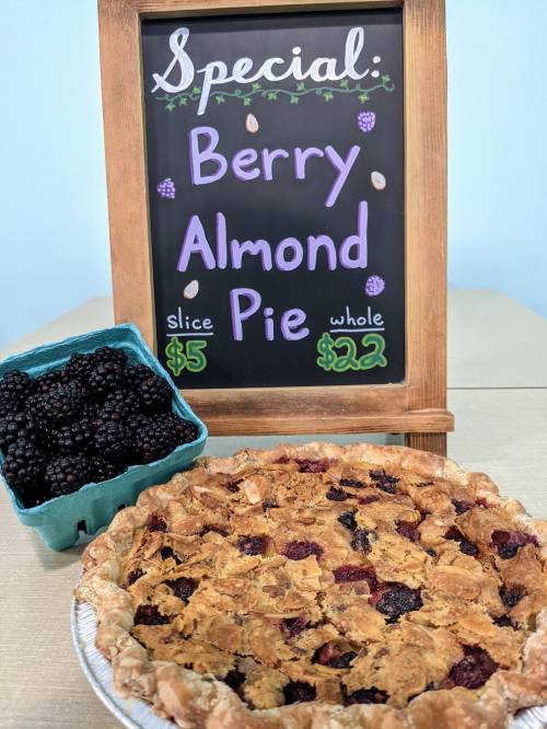 A chalkboard sign displays "Berry Almond Pie" special, with a pie and a basket of blackberries nearby.
