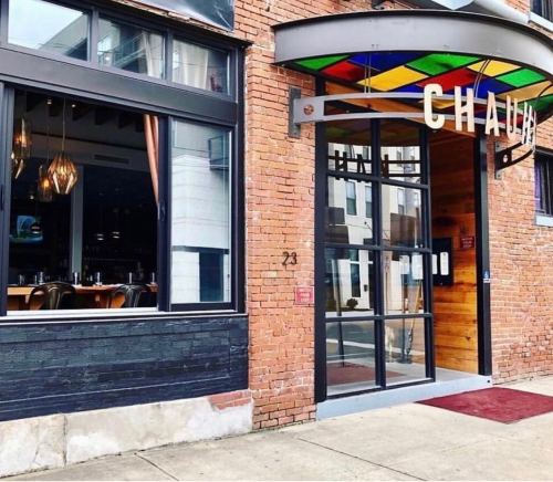 Exterior of a restaurant named "Chaja," featuring a colorful awning and large glass doors, with a brick facade.