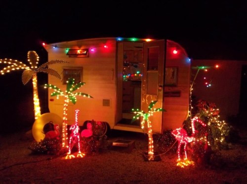 A brightly lit vintage camper decorated with colorful lights and palm tree decorations at night.