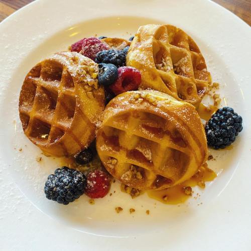 Three golden waffles topped with berries and a sprinkle of powdered sugar, served on a white plate.