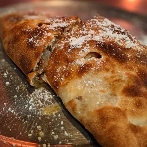 A golden-brown calzone with a crispy crust, sprinkled with flour, resting on a silver plate.