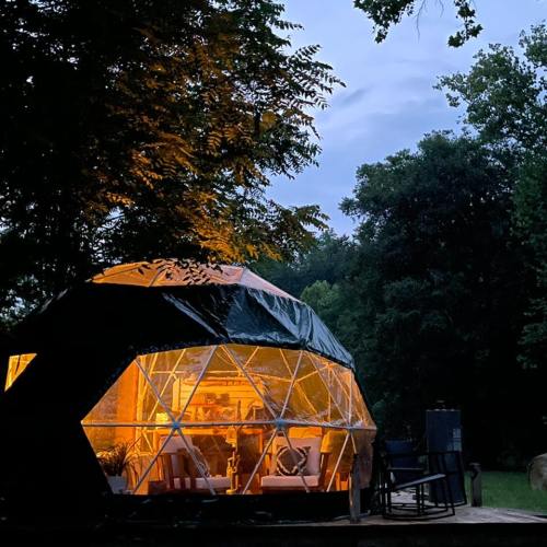 A geodesic dome cabin illuminated at dusk, surrounded by trees and nature.