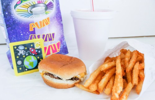 A colorful fast food meal featuring a burger, fries, a drink, and a fun-themed box.