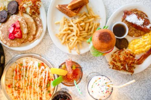 A spread of various dishes including pancakes, fries, a burger, and drinks on a table.