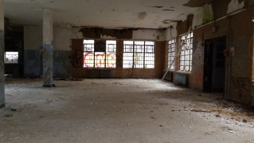 Abandoned room with peeling walls, broken windows, and graffiti, featuring debris scattered on the floor.