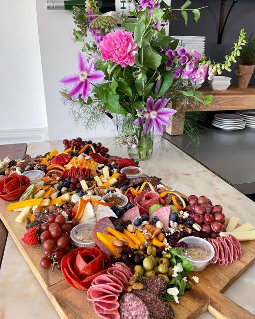 A vibrant charcuterie board with meats, cheeses, fruits, and nuts, alongside a bouquet of colorful flowers.