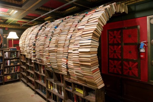 A creative bookshelf arch made of stacked books, forming a wave-like structure in a cozy library setting.