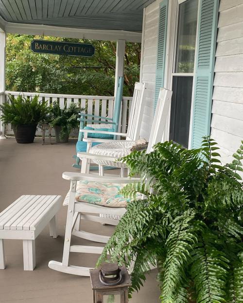 A cozy porch with rocking chairs, a small table, and ferns, featuring a sign that reads "Barclay Cottage."