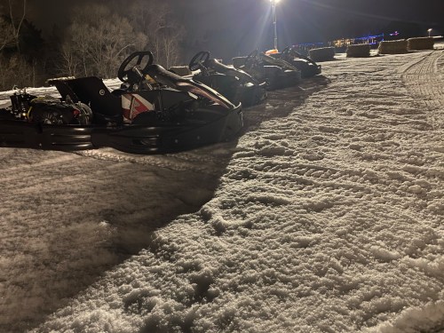 Go-karts lined up on a snowy track at night, illuminated by lights in the background.
