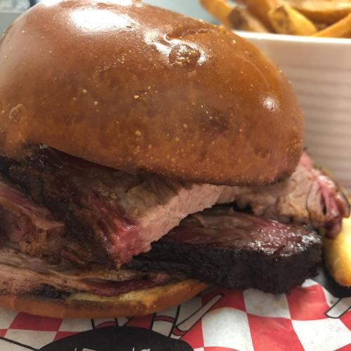 Close-up of a juicy brisket sandwich on a toasted bun, served with a side of golden fries.
