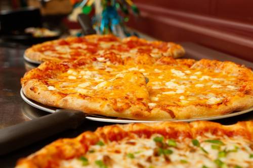 A variety of pizzas on a table, featuring cheese and toppings, ready to be served.