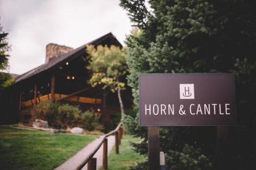 Sign for "Horn & Cantle" in front of a rustic lodge surrounded by trees and greenery.