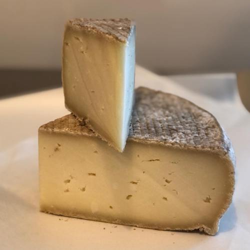A wedge of cheese with a textured rind, partially cut, resting on a light surface.