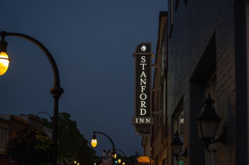 Sign for Stanford Inn illuminated at dusk, with street lamps and buildings in the background.