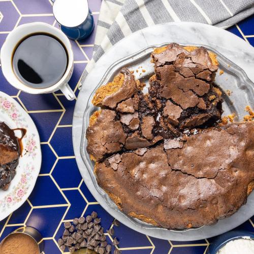 A plate of brownies next to a cup of coffee and a dessert plate on a geometric tablecloth.