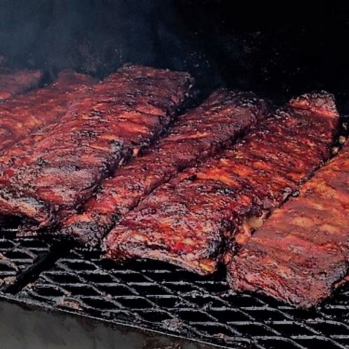 Close-up of grilled ribs on a barbecue grill, showcasing a smoky, charred texture.