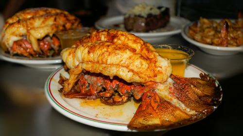A plate featuring a large, grilled lobster tail atop a whole crab, served with dipping sauces.