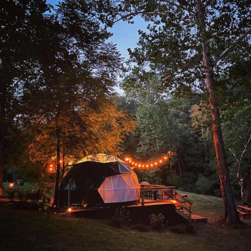 A cozy geodesic dome illuminated by string lights, surrounded by trees in a serene outdoor setting at dusk.