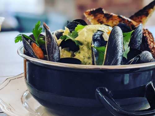 A black bowl filled with mussels, topped with herbs and accompanied by toasted bread.