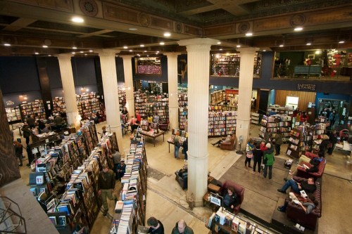 A spacious bookstore filled with shelves of books, people browsing, and cozy seating areas under grand architecture.