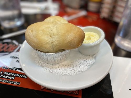 A warm, golden-brown roll shaped like a heart, served with a small dish of butter on a white plate.