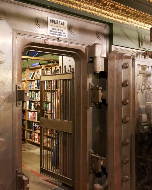 A large, metallic vault door labeled "Horror Vault" opens to reveal shelves filled with books inside.