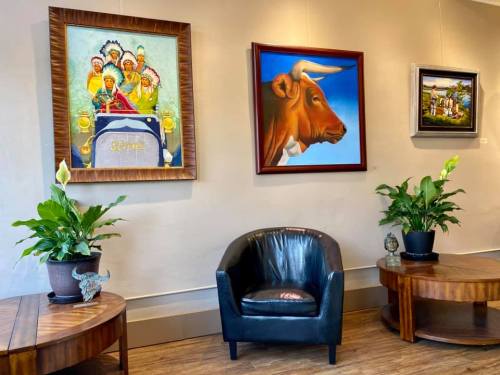A cozy seating area featuring two wooden tables, a black chair, and colorful artwork on the walls, surrounded by plants.
