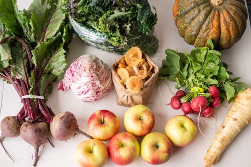 A variety of fresh vegetables and fruits, including beets, radishes, apples, kale, and a pumpkin, arranged on a table.