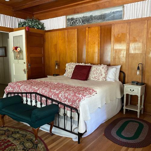 Cozy bedroom with wooden walls, a bed with a red and white quilt, a nightstand, and a green bench at the foot of the bed.