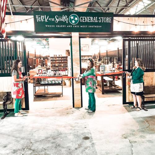Three women in festive attire cut a ribbon at the Fork of the South General Store, celebrating its opening.