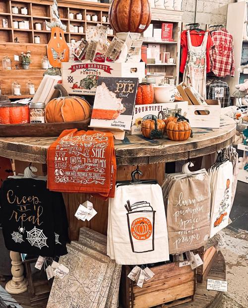 A rustic display featuring pumpkins, fall-themed towels, and decor items on a wooden table in a cozy shop.