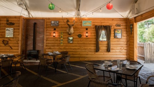 Cozy wooden dining area with tables, rustic decor, and warm lighting, featuring a stove and camp-themed wall art.
