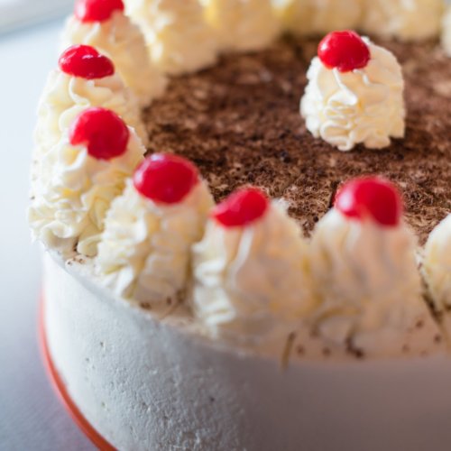 A round cake topped with whipped cream peaks and cherries, with a chocolate sprinkle layer in the center.