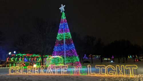 A brightly lit Christmas tree with colorful lights, surrounded by festive decorations and the words "CELEBRATE THE LIGHT."