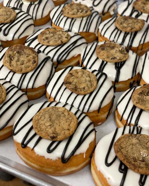 A close-up of donuts topped with white icing, chocolate drizzle, and a cookie on each.