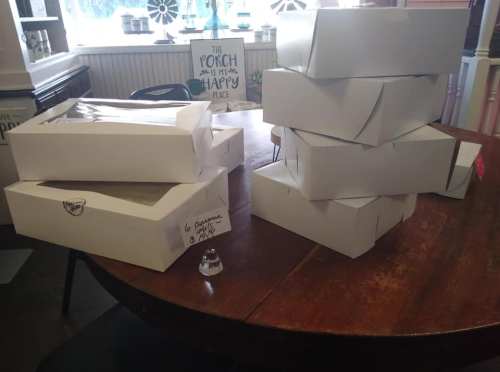 A stack of white boxes on a wooden table, with a small glass object in front and a sign in the background.