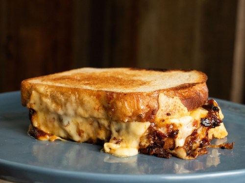 A toasted sandwich with melted cheese and a rich filling, served on a blue plate.