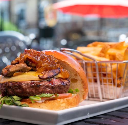 A juicy burger topped with mushrooms and caramelized onions, served with a side of golden fries in a basket.
