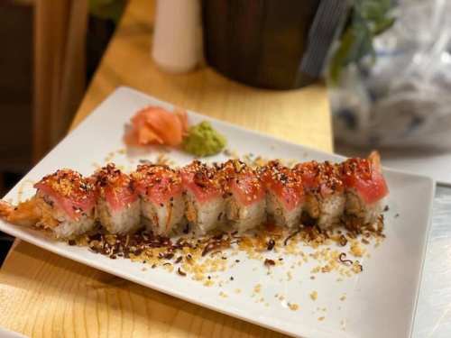 A plate of sushi rolls topped with tuna, sesame seeds, and garnished with wasabi and pickled ginger.