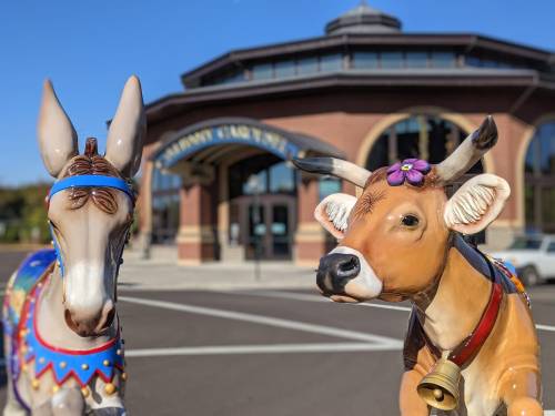 Two colorful animal sculptures, a donkey and a cow, in front of a large building with a curved roof.